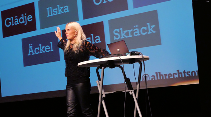 Therese Albrechtson står på scenen i Partille Gymnasiums aula. Vid sidan står ett bord med en dator på. Therese Albrechtson står på scenen i Partille Gymnasiums aula. Vid sidan står ett bord med en dator på.